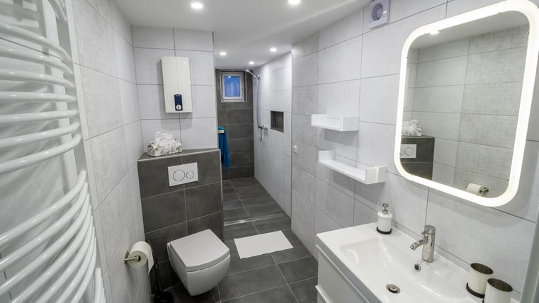 Ein modernes Badezimmer mit weißen Fliesen und eleganten Möbeln. Es gibt eine Dusche, ein Waschbecken und eine Toilette.