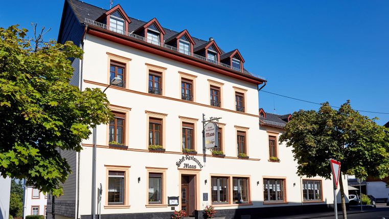 Ein schönes historisches Gebäude mit einem hellen Fassaden und roten Dachfenstern. Umgeben von Bäumen und einem blauen Himmel.