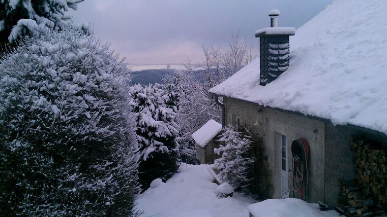 Ein verschneites Winterlandschaft mit einem kleinen Haus und schneebedeckten Bäumen. Die Szene wirkt ruhig und idyllisch.