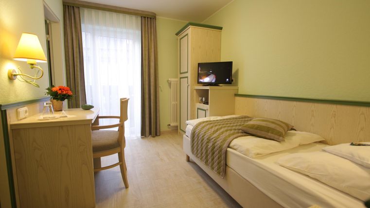 Ein gemütliches Zimmer mit einem Einzelbett und einem Schreibtisch. Große Fenster sorgen für viel Tageslicht und eine angenehme Atmosphäre.