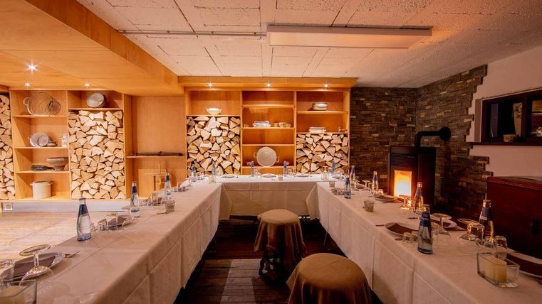 Ein gemütliches Esszimmer mit Holzregalen und einer Feuerstelle. Tische sind bereit für Gäste, umgeben von warmem Licht.