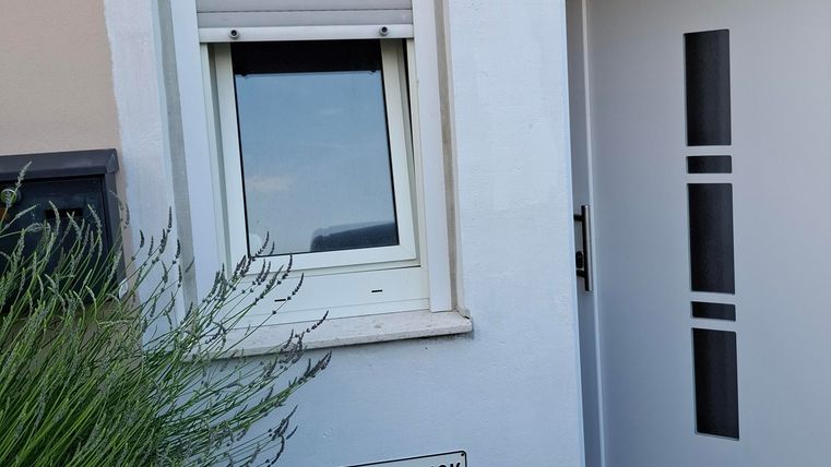 Ein modernes Haus mit einem klaren, weißen Eingangsbereich und einem Fenster. Vor dem Haus steht ein Schild mit der Aufschrift "Phaus Waldblick".