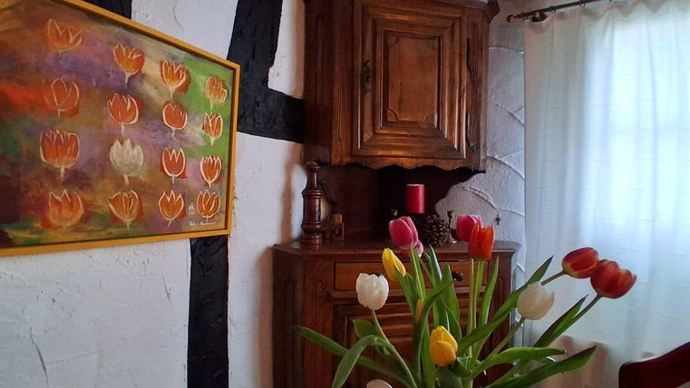 Ein gemütlicher Raum mit einem Holzkasten und einem bunten Gemälde von Tulpen. Auf dem Tisch steht eine Vase mit frischen Tulpen in verschiedenen Farben.