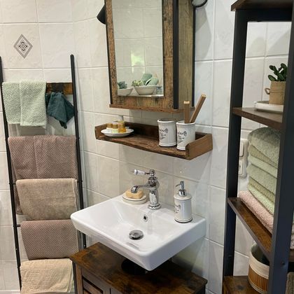 Ein modernes Badezimmer mit einem weißen Waschbecken und einem Holzspiegel. Im Hintergrund sind Handtücher und dekorative Elemente auf Regalen zu sehen.