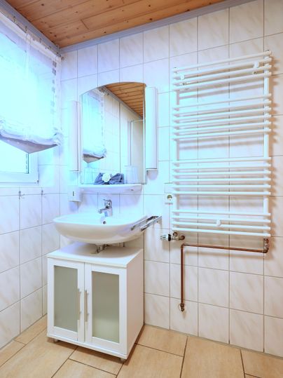 Ein modernes Badezimmer mit einem Waschbecken und einem großen Spiegel. Die Wände sind gefliest, und ein Handtuchheizkörper ist an der Wand befestigt.