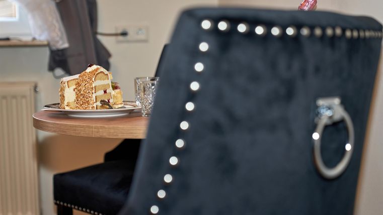 Ein schöner Tisch mit einem Stück Kuchen und einem Glas. Im Hintergrund ist ein stilvoller Stuhl sichtbar.