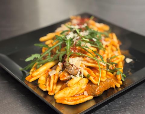 Ein Teller mit Pommes, garniert mit Fleischstücken und frischen Kräutern. Die Speise ist mit einer roten Sauce dekoriert.