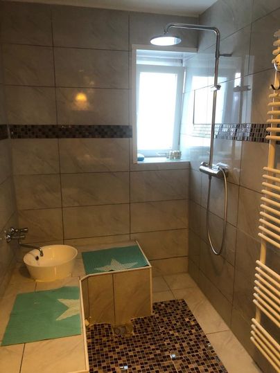 Ein modernes Badezimmer mit Dusche und Fenster. Die Wände sind mit hellen Fliesen verkleidet und es gibt einen Handtuchwärmer.