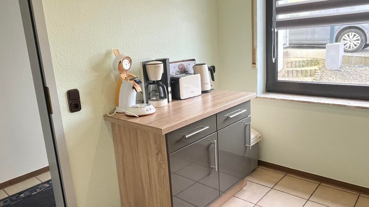 Eine moderne Küche mit einem Holzschrank und verschiedenen Küchengeräten. Das Fenster bietet viel Tageslicht und einen Blick nach draußen.