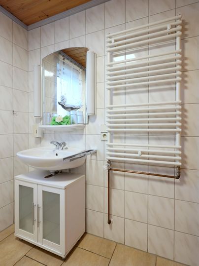 Ein modernes Badezimmer mit einem Waschbecken und einem großen Spiegel. Neben dem Waschbecken befindet sich ein Handtuchheizkörper an der Wand.