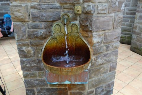 Ein antiker Brunnen aus Metall mit fließendem Wasser. Der Brunnen ist in eine Steinmauer integriert.