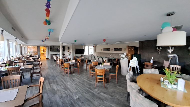 Ein modernes Restaurant mit Holzmöbeln und großen Fenstern. Der Raum ist hell und freundlich, dekoriert mit bunten Elementen.