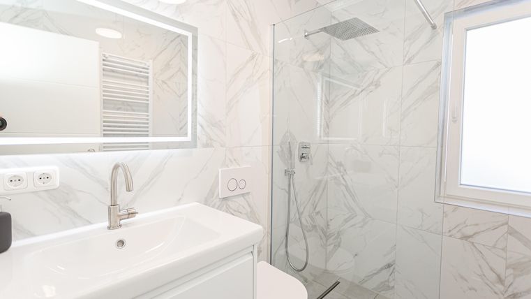Ein modernes Badezimmer mit hellem Marmor-Look und einer begehbaren Dusche. Der Waschbeckenbereich ist sauber und gut beleuchtet.