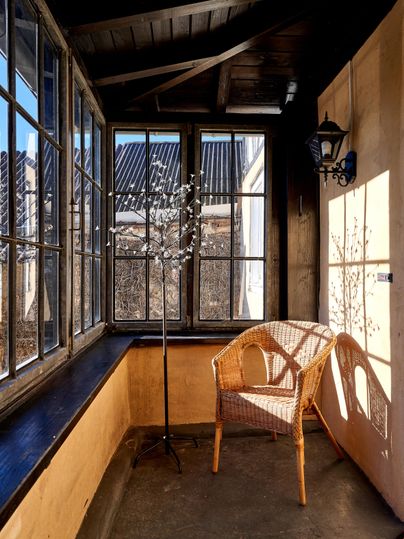 Eine gemütliche Veranda mit großen Fenstern und einem Korbsessel. Das Licht fällt sanft auf den Boden und die Wände.