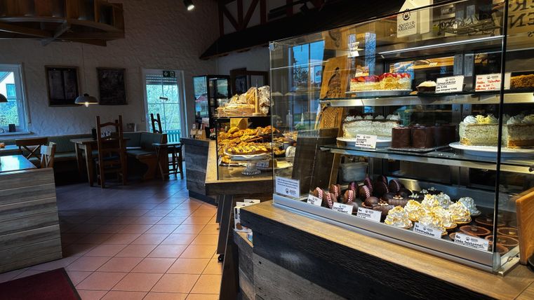 Ein gemütliches Café mit einer Vitrine voller Leckereien. Der Innenraum ist einladend und hell.
