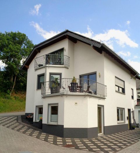 Ein modernes Haus an einer ruhigen Straße. Es hat mehrere Balkone und ist von Bäumen umgeben.