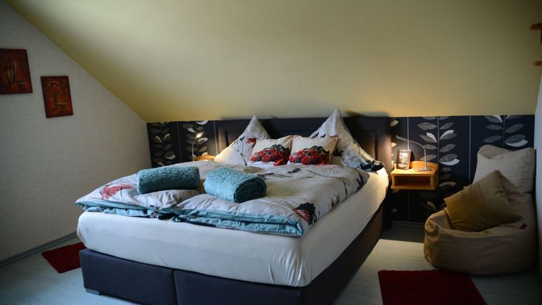 Ein gemütliches Schlafzimmer mit einem großen Bett, dekorativen Kissen und sanftem Licht. Eine Ecke mit einem Sitzsack und stilvollen Wanddekoren sorgt für eine einladende Atmosphäre.