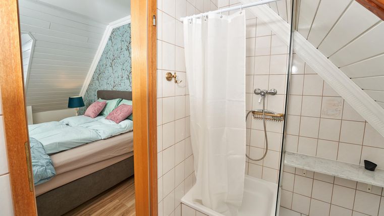 Ein modernes Badezimmer mit einer Dusche und angrenzendem Schlafzimmer. Die Wände sind hell gefliest und es gibt eine gemütliche Atmosphäre.