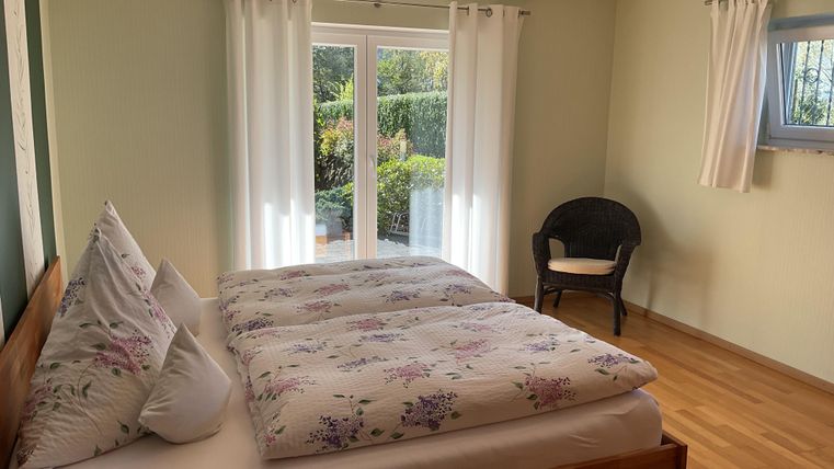 Ein gemütliches Schlafzimmer mit einem Doppelbett und Blick auf den Garten. Die großen Fenster lassen viel Licht herein und sorgen für eine angenehme Atmosphäre.