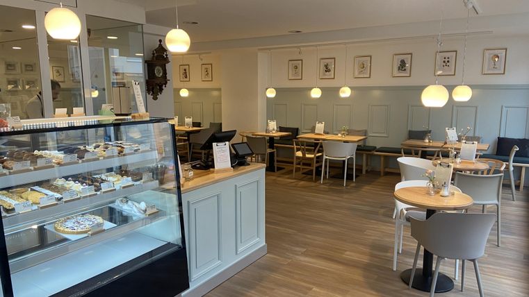 Ein modernes Café mit einer Vitrine voller Köstlichkeiten. Die Einrichtung ist hell und freundlich, mit gemütlichen Sitzplätzen.