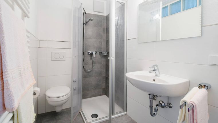 Ein modernes Badezimmer mit einer Dusche, einem Waschbecken und einer Toilette. Die Wände sind hell und es gibt Handtücher in sanften Farben.