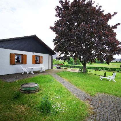 Ein gemütliches Haus mit einem großen Baum im Garten. Die Umgebung ist grün und einladend, ideal zum Entspannen.