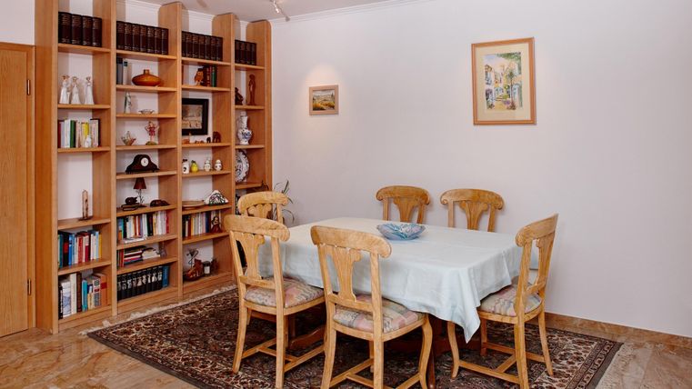 Ein einladender Essbereich mit einem runden Tisch und sechs Stühlen. Im Hintergrund befindet sich ein Bücherregal mit verschiedenen Büchern und dekorativen Objekten.