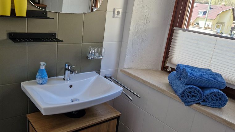 Ein modernes Badezimmer mit einem Waschbecken und einem großen Spiegel. Handtücher und Toilettenartikel sind ordentlich angeordnet.