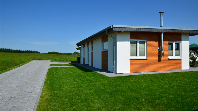 Ein modernes Einfamilienhaus mit einer Kombination aus Holz- und Putzfassade. Der Garten ist gepflegt und von einer grünen Wiese umgeben.
