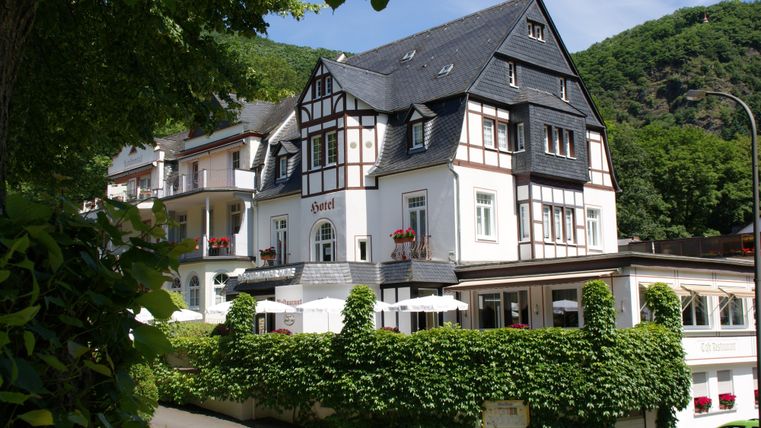 Ein charmantes Fachwerkhaus umgeben von grünen Pflanzen. Die Umgebung zeigt sanfte Hügel und eine einladende Atmosphäre.