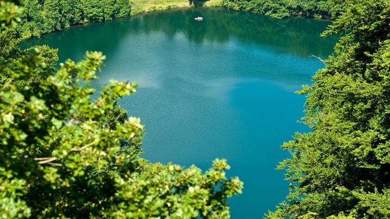 Ein ruhiger See umgeben von üppigem Grün. Das Wasser hat eine wunderbare blaue Farbe und spiegelt die Natur wider.