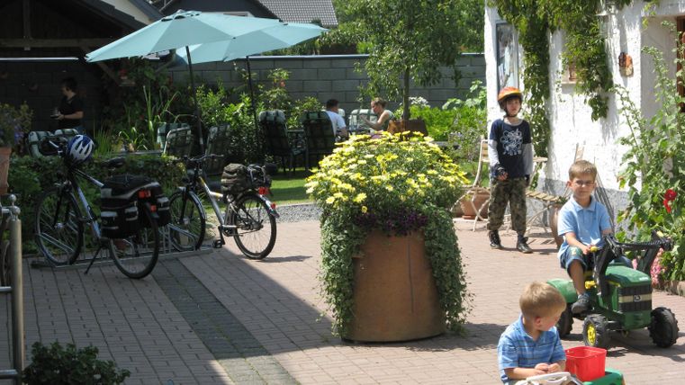Ein hübscher Innenhof mit Pflanzen und Spielzeug für Kinder. Im Hintergrund sind Fahrräder und eine Sonnenschirm.