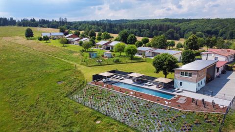 Eine ruhige Landschaft mit einem modernen Haus und einem Pool. Im Hintergrund sind mehrere kleinere Gebäude und viel Grün zu sehen.
