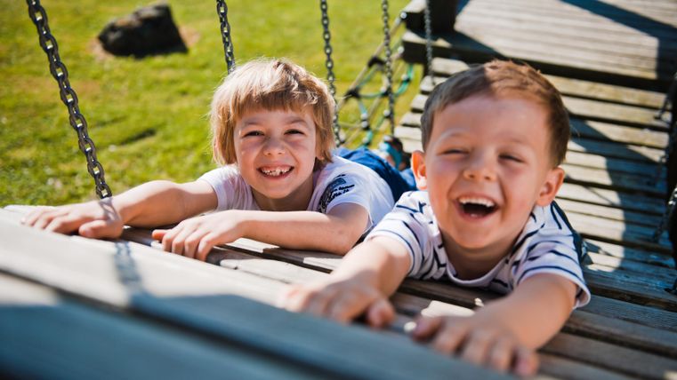 Zwei lachende Kinder liegen auf einer Schaukel und haben Spaß. Sie genießen einen sonnigen Tag im Freien.