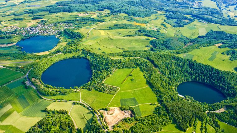 Eine Luftaufnahme von grünen Feldern und zwei blauen Seen. Die Landschaft zeigt sanfte Hügel und Wälder in der Umgebung.