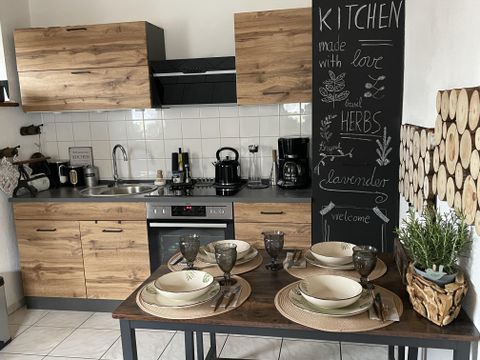 Eine moderne Küche mit Holzregalen und einem Essbereich. Der Tisch ist gedeckt mit Geschirr und dekorativen Pflanzen.