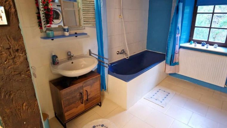 Ein modernes Badezimmer mit blauen Akzenten und einer Badewanne. Es gibt ein Waschbecken, einen Spiegel und ein Fenster mit Ausblick.