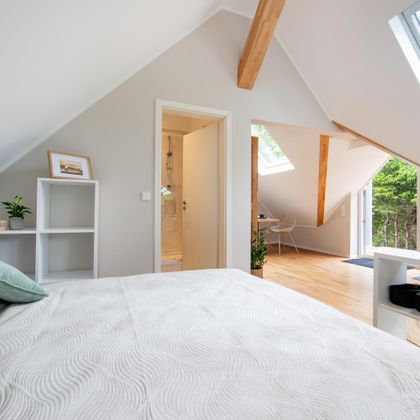 Ein modernes Schlafzimmer mit schrägen Wänden und Holzdetails. Es gibt Fenster, die viel Licht reinlassen und einen Blick ins Freie bieten.