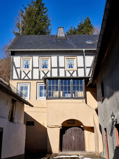 Ein traditionelles Fachwerkhaus mit einer Kombination aus Holz- und Steinverkleidung. Der Himmel ist klar und die Umgebung ist ländlich.