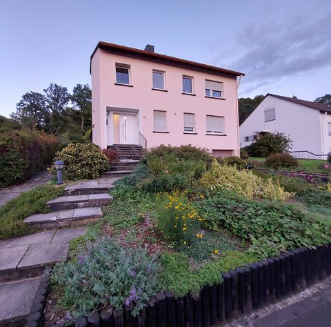 Ein modernes Haus mit einer hellen Fassade und mehreren Fenstern. Der Vorgarten ist üppig bepflanzt und gut gepflegt.