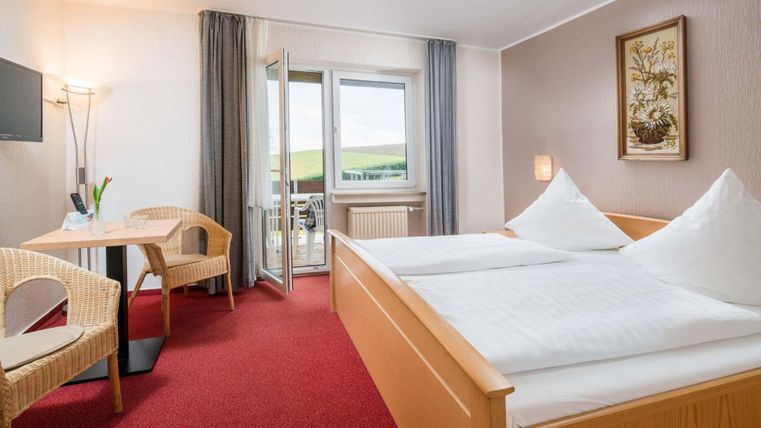 Ein gemütliches Hotelzimmer mit zwei Einzelbetten. Es gibt einen Tisch, zwei Stühle und einen Balkon mit Blick auf die Landschaft.