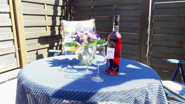 Ein schöner Tisch im Freien mit einem Flasche Wein und zwei Gläsern. Eine kleine Vasen mit bunten Blumen steht ebenfalls auf dem Tisch.
