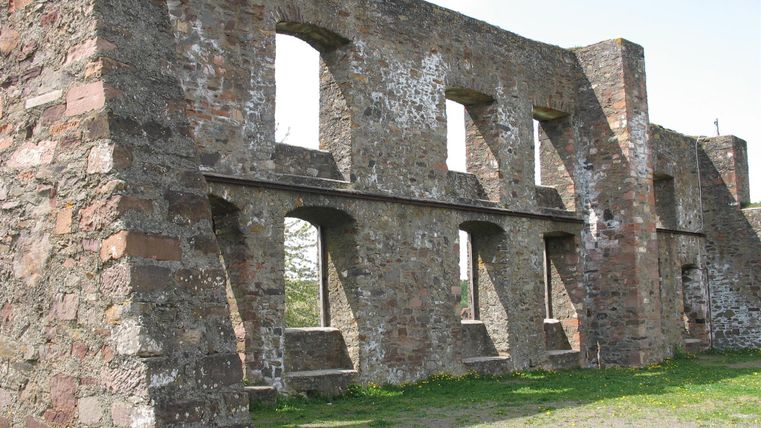 Eine alte Ruine mit steinernem Mauerwerk und offenen Fenstern. Der grüne Rasen umgibt die Struktur und vermittelt ein Gefühl von Geschichte.