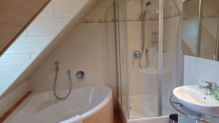 Ein modernes Badezimmer mit einer Badewanne und einer separaten Dusche. Es gibt auch ein Waschbecken und großzügige Fenster für viel Licht.