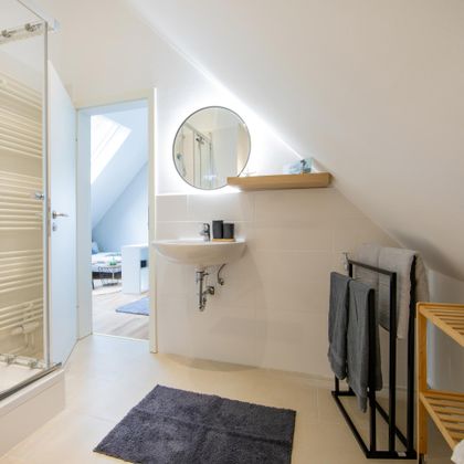 Ein modernes Badezimmer mit einer Dusche und einem Spiegel. Holzregale und Handtücher verleihen dem Raum eine gemütliche Atmosphäre.