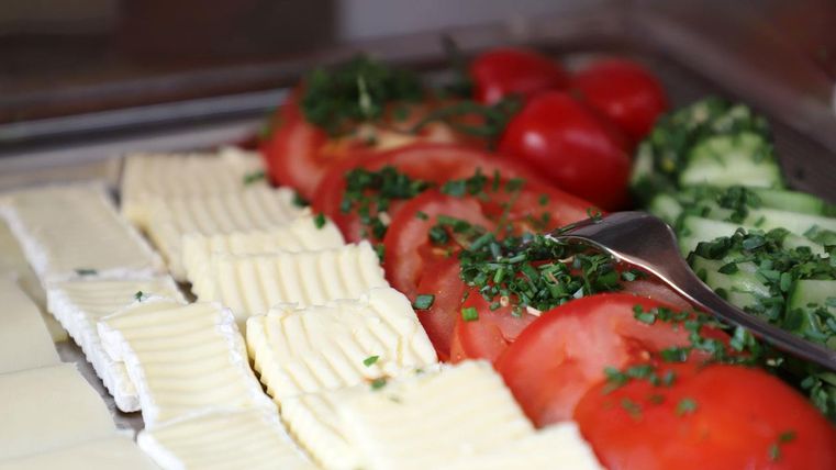 Eine frische Auswahl an Lebensmitteln mit geschnittenen Tomaten, Gurken und Butter. Die Zutaten sind mit frischem Schnittlauch garniert.