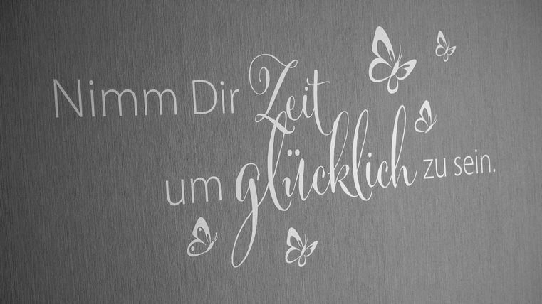 Ein inspirierendes Zitat auf einer Wand. Es ermutigt, sich Zeit zu nehmen, um glücklich zu sein.