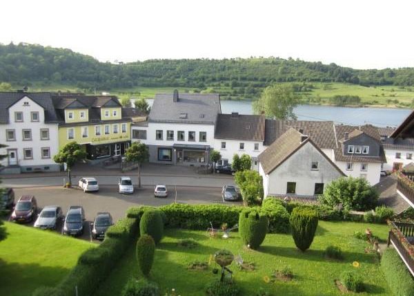 Eine malerische Aussicht auf eine kleine Stadt am Fluss. Die Gebäude sind von gepflegten Gärten umgeben und die Landschaft ist grün und einladend.
