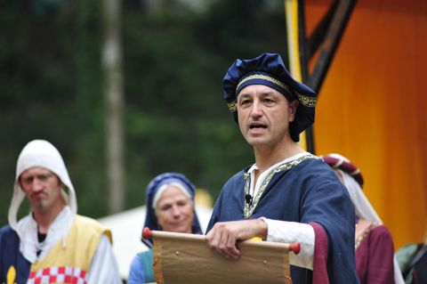 Een historische gebeurtenis met een spreker in middeleeuwse kledij. Op de achtergrond zijn andere personen in traditionele kostuums te zien.