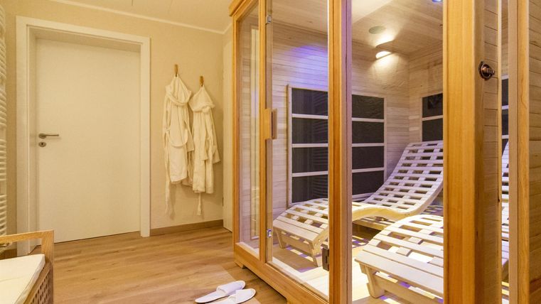 Ein entspannender Bereich mit einer Sauna und Liegen. Weiße Bademäntel hängen an der Wand und der Raum ist hell beleuchtet.